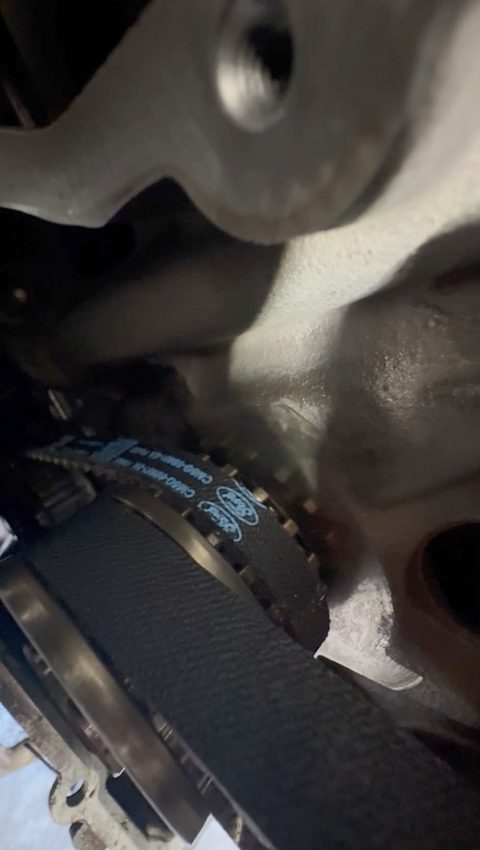 Close-up of a Ford-branded wet belt under the engine during a wet belt replacement at AGR Performance, Stafford