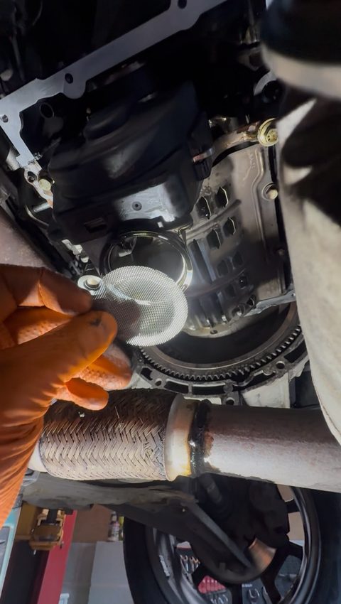 View from underneath with the sump removed, a gloved hand holding the oil pick-up mesh strainer, at AGR Performance, Stafford