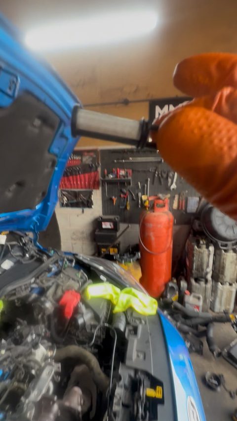 Gloved hand holding an oil pick-up strainer removed for inspection, with the bonnet up in the AGR Performance workshop, Stafford